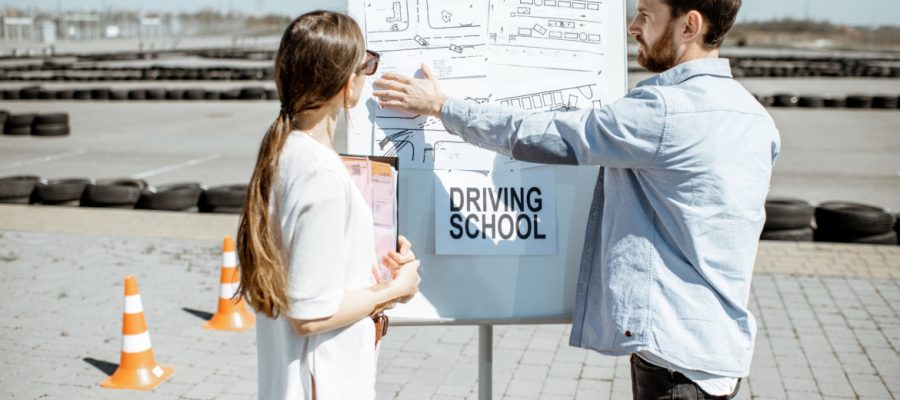 Male instructor showing traffic shemes to a young female student standing on the training ground at the driver's school